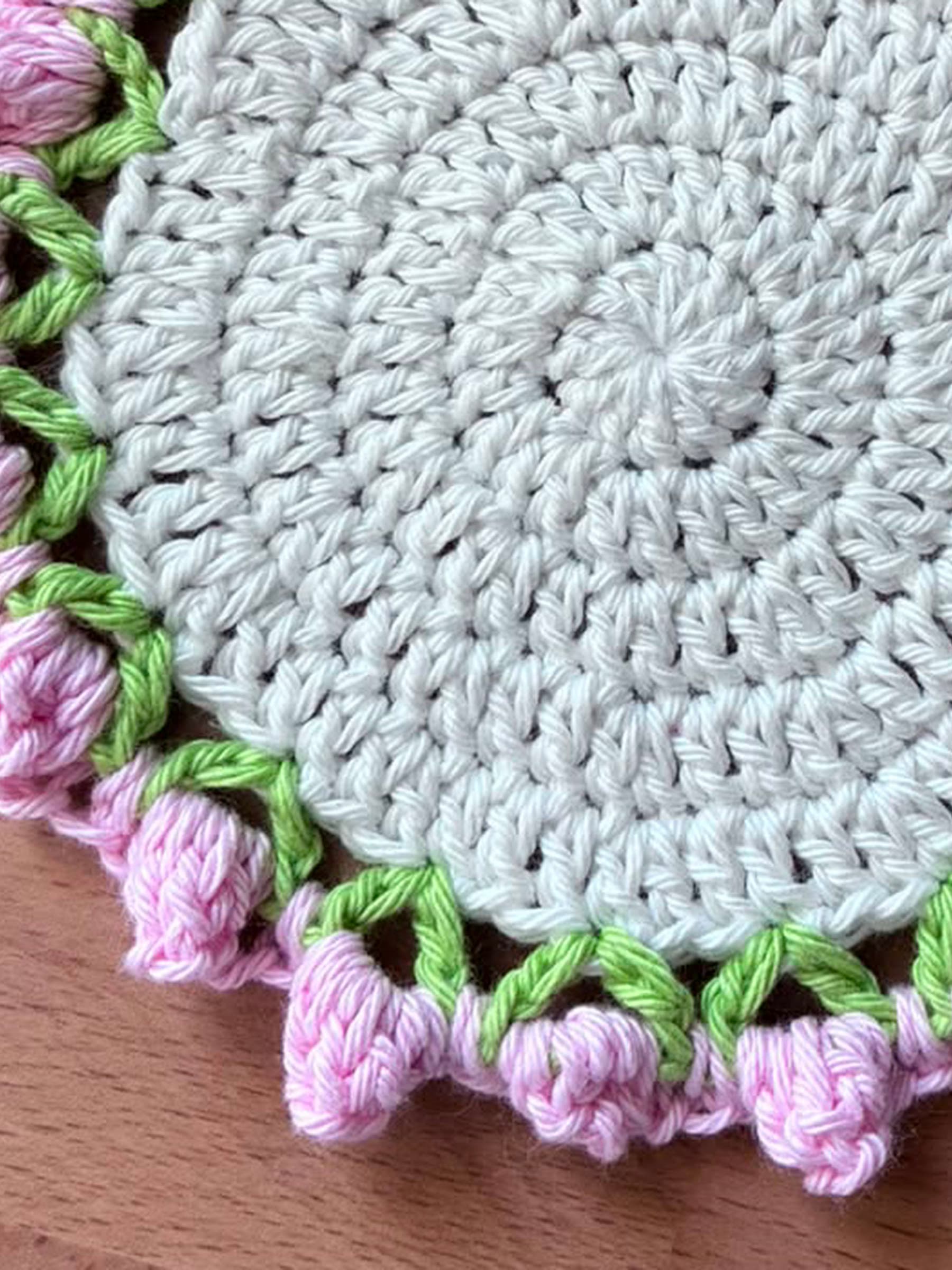 Close up of the crochet stitches, pink rosebuds and green leaf edging